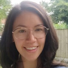 Portrait of Tabitha Ha wearing glasses, dark brown hair, with a fence and greenery on the background